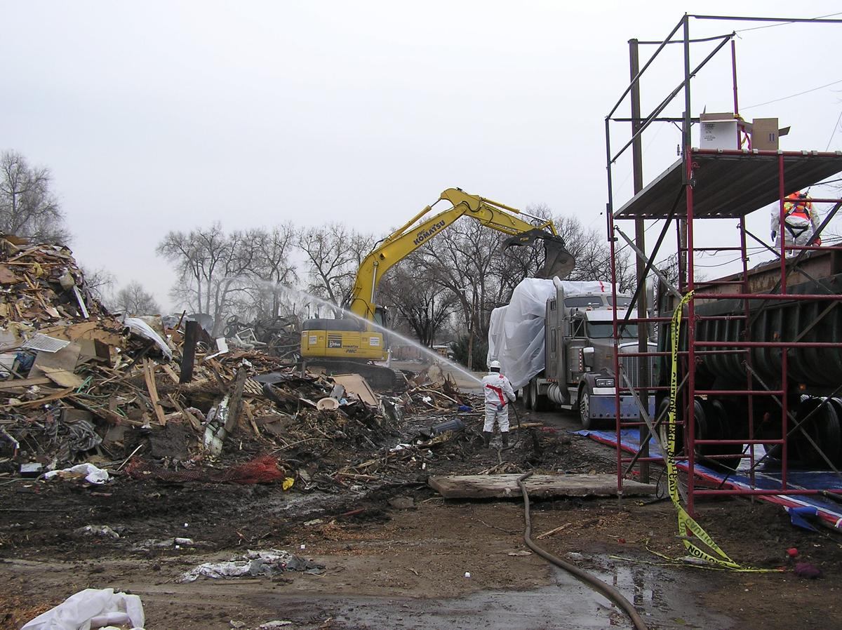 Hazmat crew loading debris behind containment on a remediation site