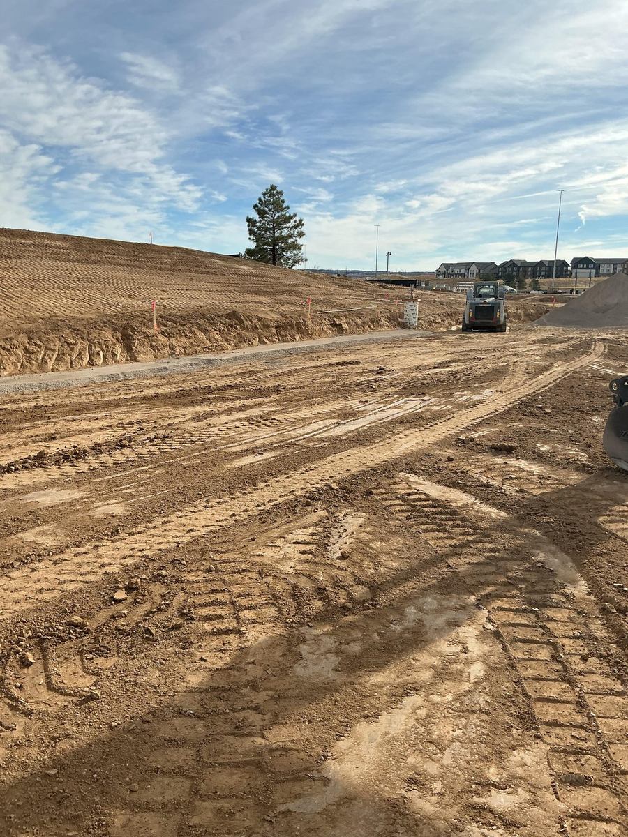 Skid steer fine-grading a building pad with new gravel access road