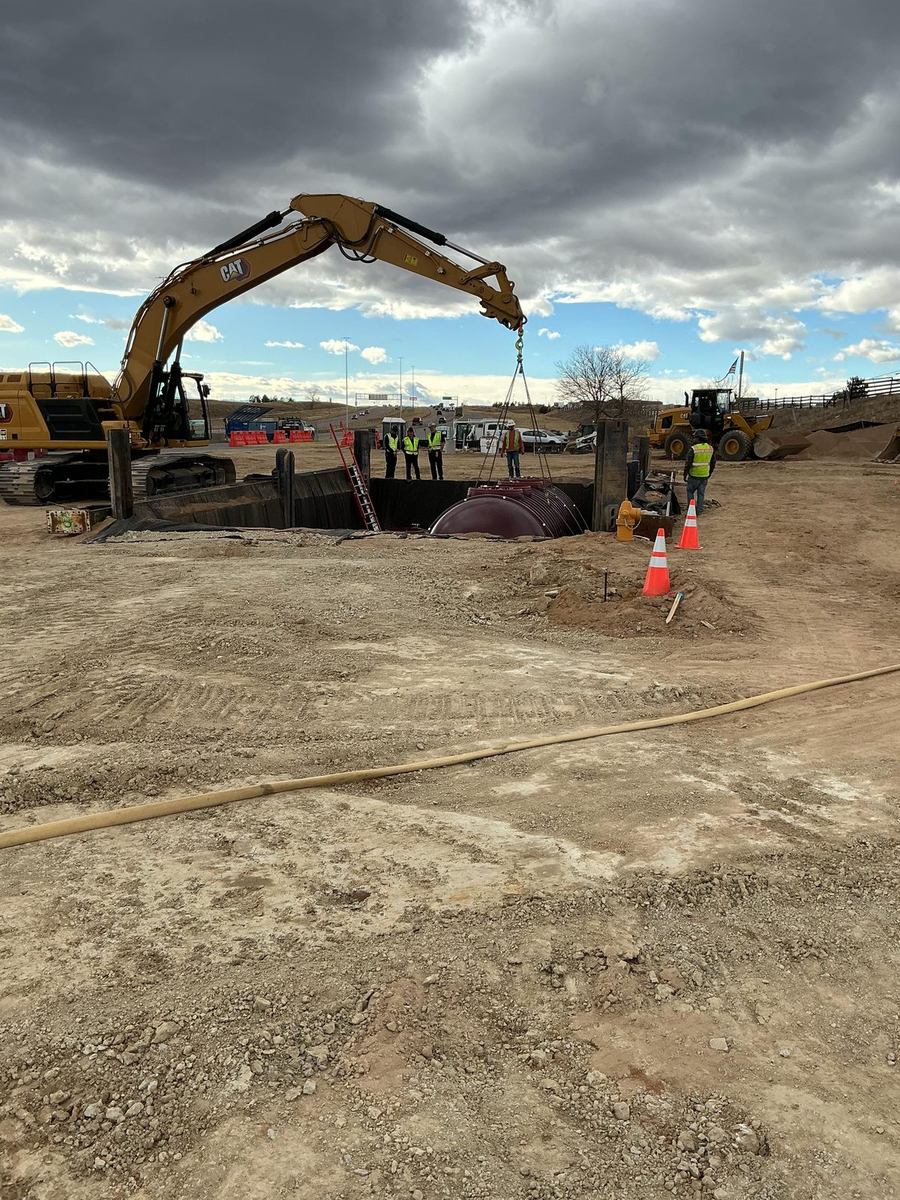 Excavator and crane rigging lowering a fuel tank into the excavation