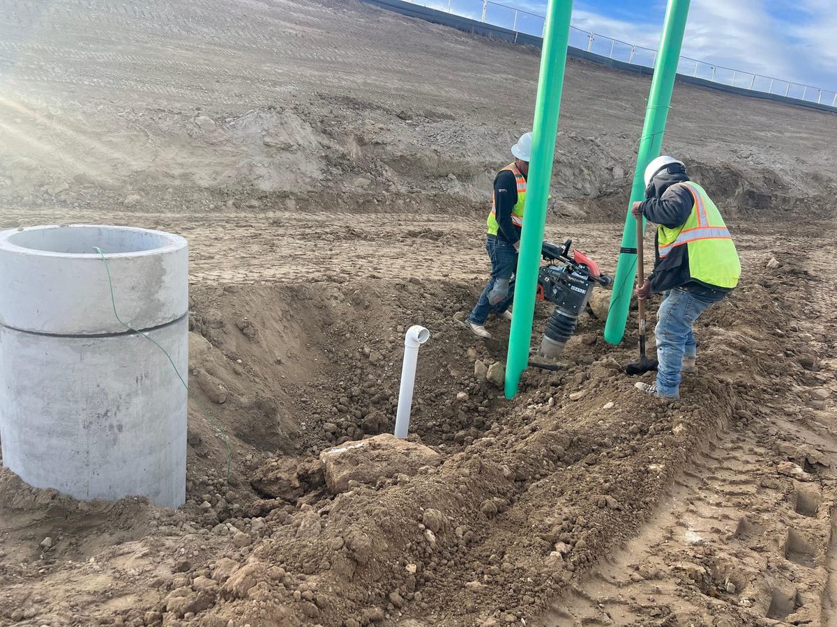 Crew compacting backfill around the interceptor risers with a jumping-jack compactor
