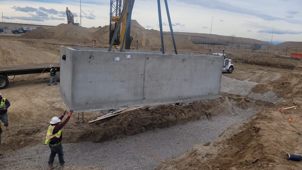 Crane lifting a large precast concrete grease interceptor vault over the excavation