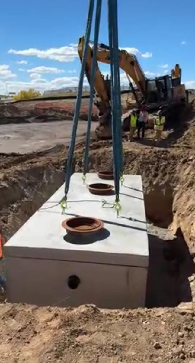 Crane lowering a precast grease interceptor box with access risers