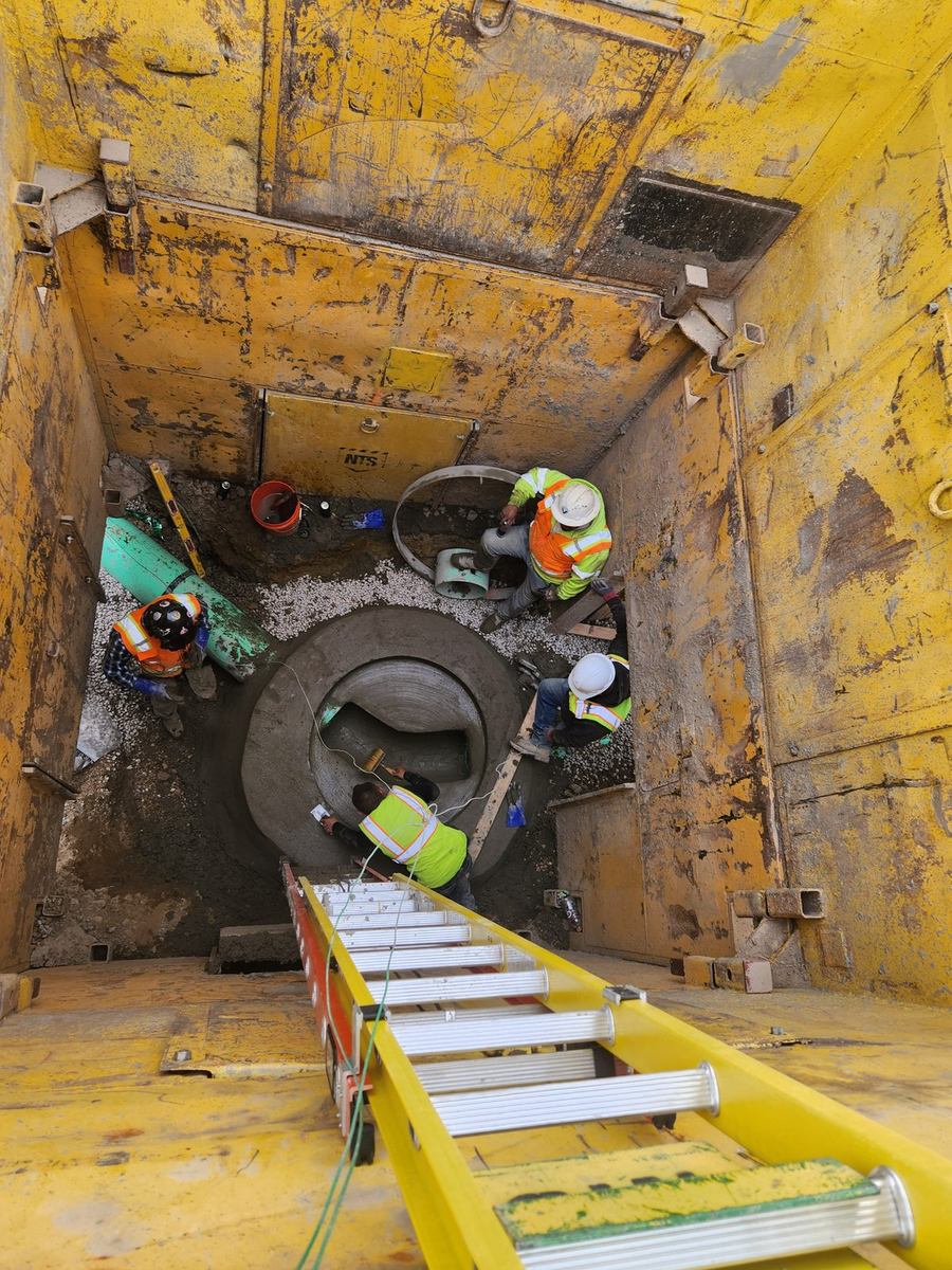 Crew setting a cast-in-place manhole base in a shored excavation