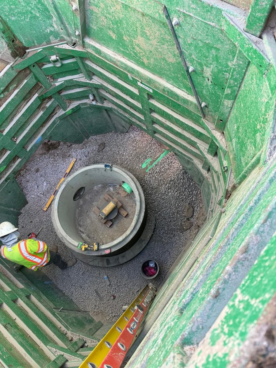 Cast-in-place manhole base set inside green trench-shoring box