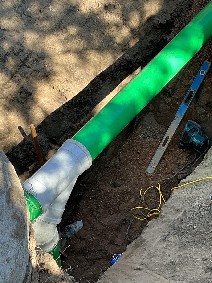Close-up of a green sewer main with a white wye fitting in the trench