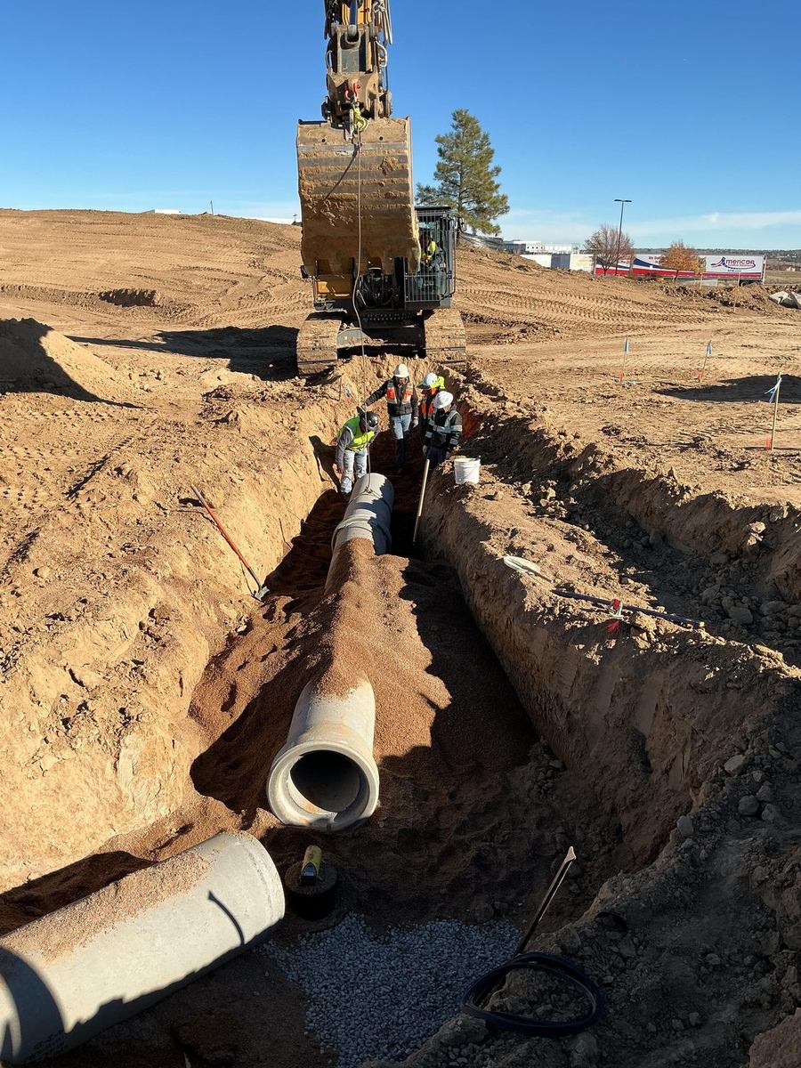 Excavator lowering large-diameter RCP storm pipe into a trench with crew