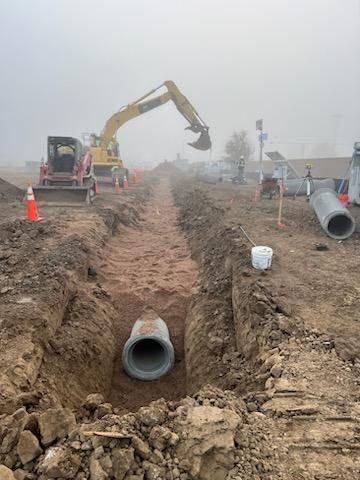 Installing RCP storm pipe in an open trench with excavator and skid steer