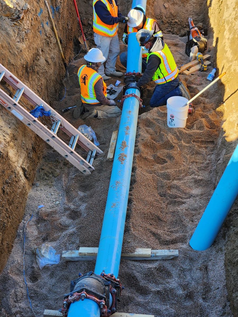 Crew assembling large-diameter C-900 water main with mechanical-joint fittings in a shored trench