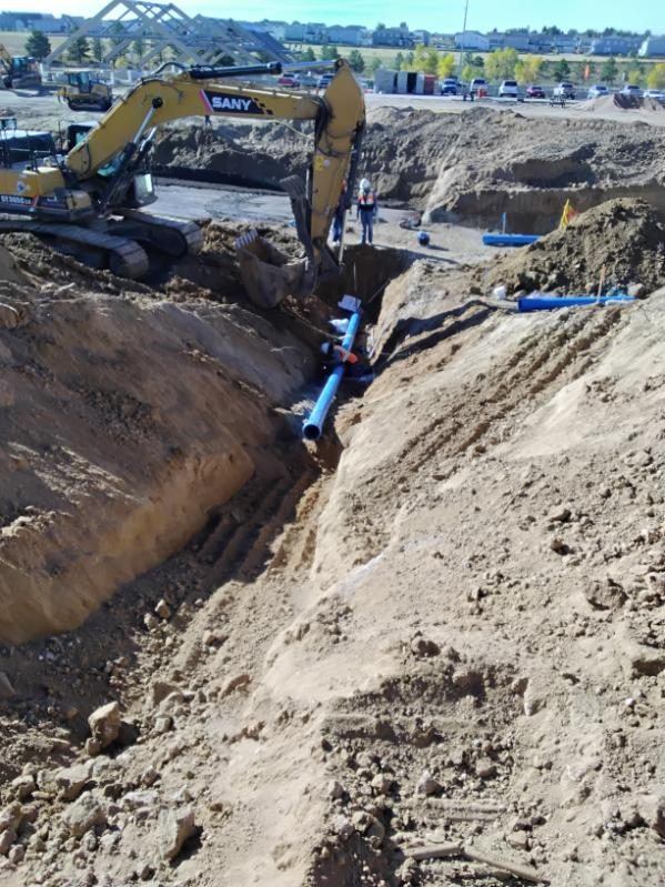 SANY excavator lowering blue C-900 pipe into a deep trench
