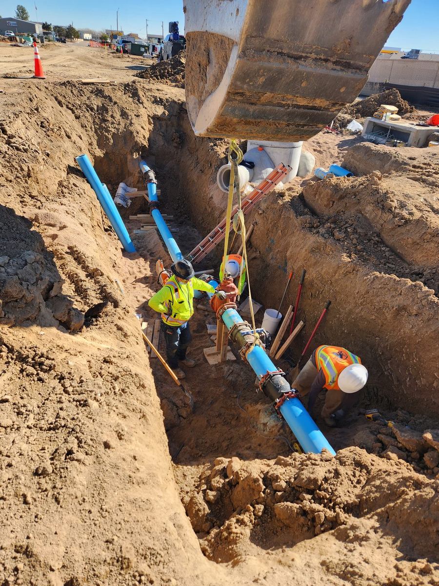 Excavator and crew lowering a large-diameter C-900 water main into the trench